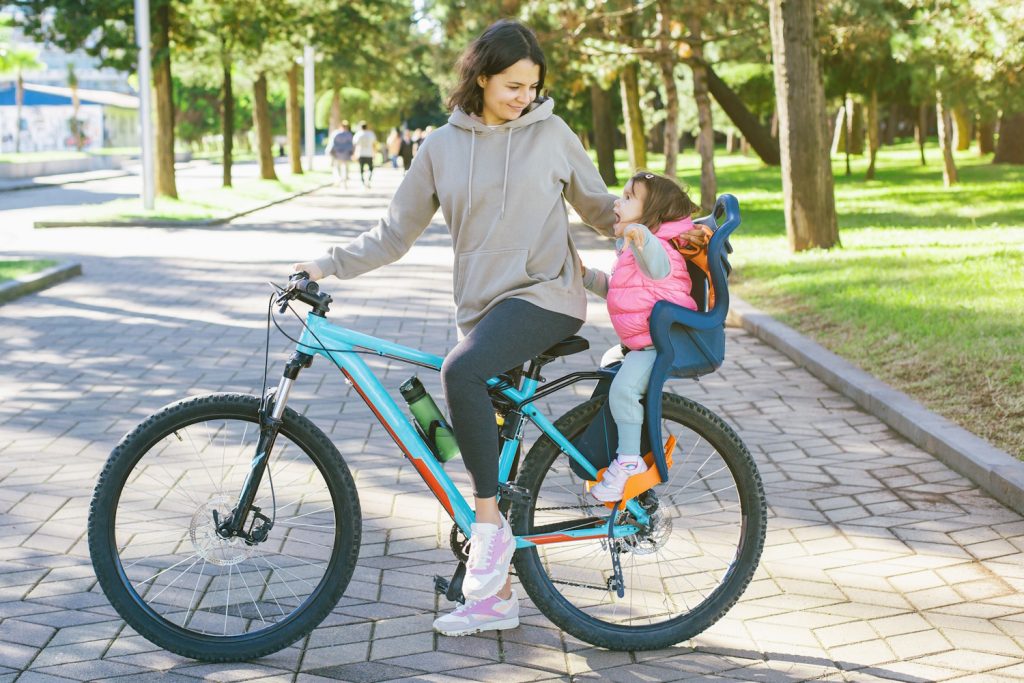anyuka biciklin, mögötte bidiklis gyerekülésen a kislánya