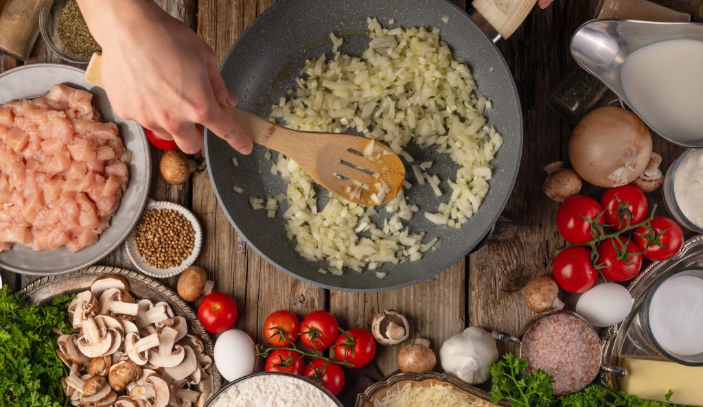 hagyma dinsztelődik serpenyőben, melette egy jó vacsora hozzávalói, csirkemell, paradicsom, fűszerek