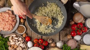 hagyma dinsztelődik serpenyőben, melette egy jó vacsora hozzávalói, csirkemell, paradicsom, fűszerek