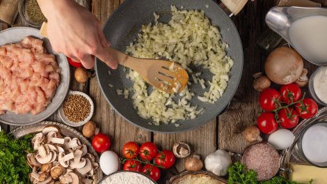 hagyma dinsztelődik serpenyőben, melette egy jó vacsora hozzávalói, csirkemell, paradicsom, fűszerek