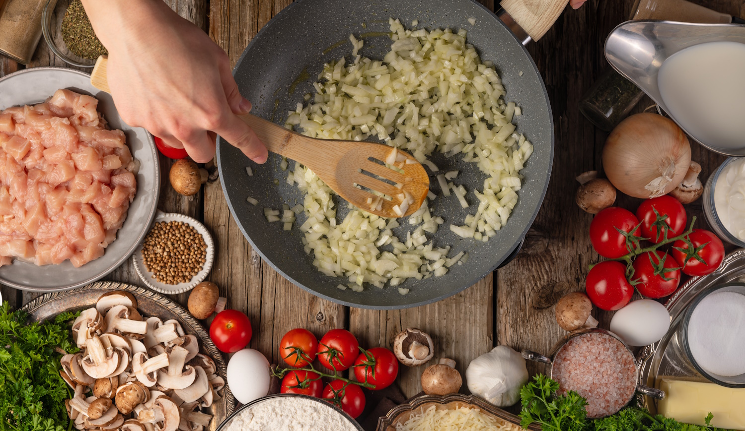 hagyma dinsztelődik serpenyőben, melette egy jó vacsora hozzávalói, csirkemell, paradicsom, fűszerek