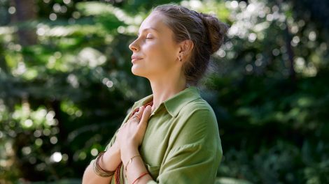 Egy nő csukott szemmel, mellkasára tett karral gyakorolja a tudatos jelenlétet