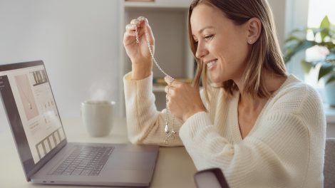 Fiatal nő az interneten rendelt ékszerrel a kezében laptop előtt
