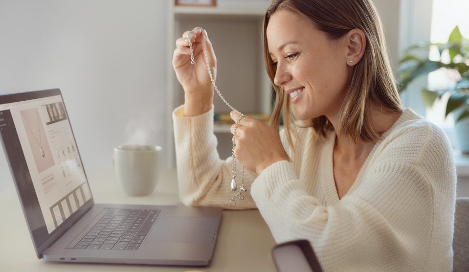 Fiatal nő az interneten rendelt ékszerrel a kezében laptop előtt