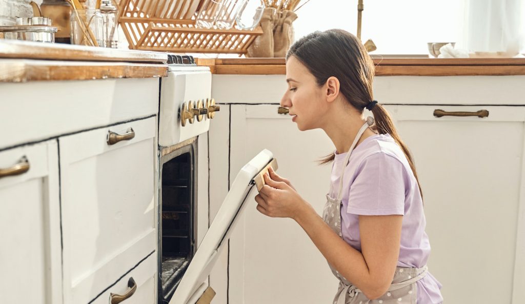 nő néz be a sütőbe egy vintage konyhában, hogy ksz van-e már a vacsora