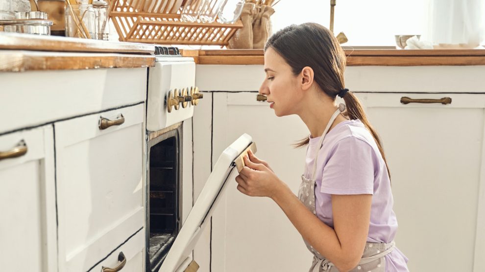 nő néz be a sütőbe egy vintage konyhában, hogy ksz van-e már a vacsora