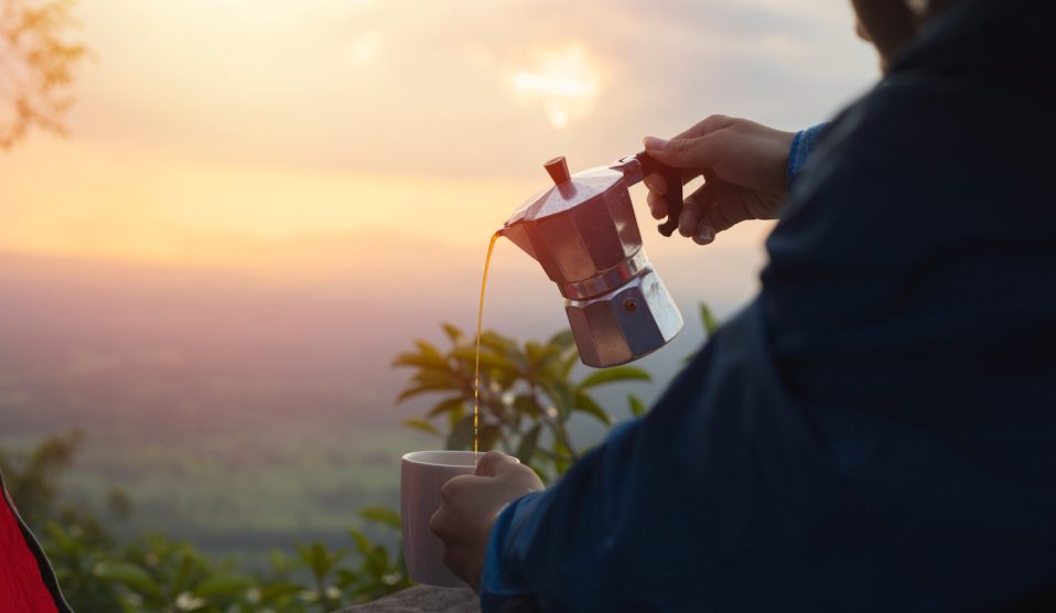 kotyogósból kávét tölt ki egy férfi napfelkeltében