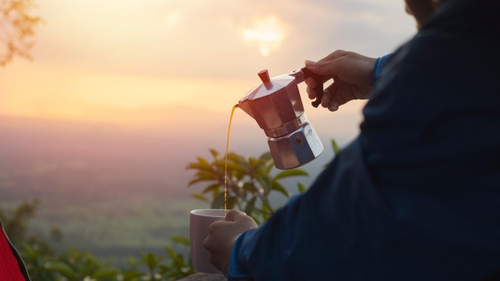 kotyogósból kávét tölt ki egy férfi napfelkeltében