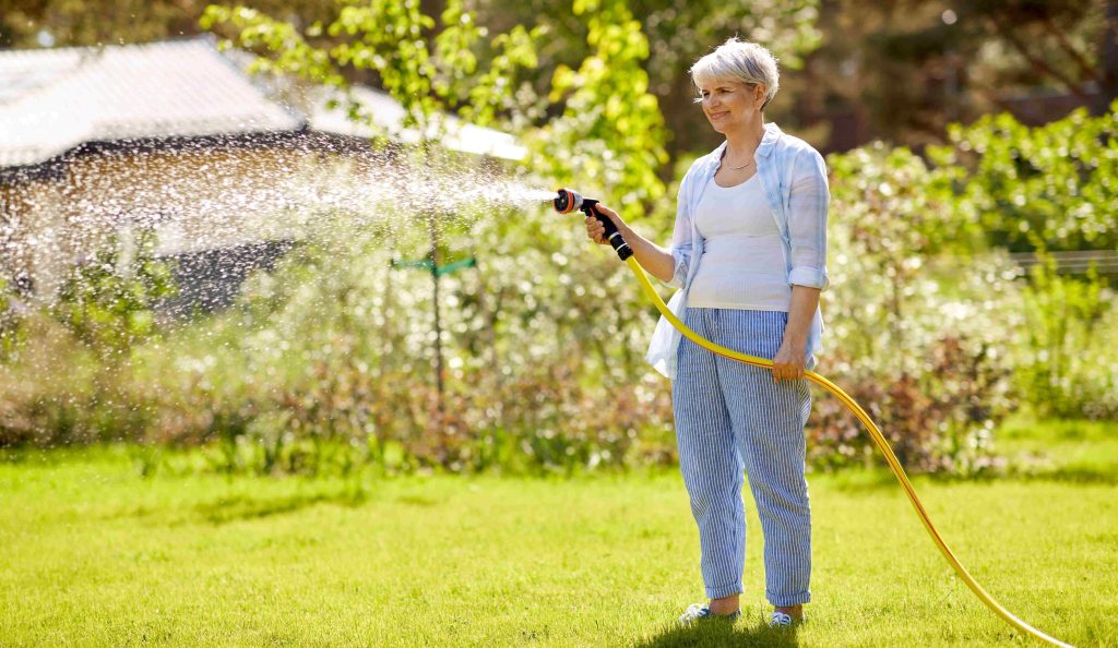 középkorú nő locsolja a füvet