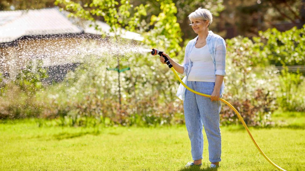 középkorú nő locsolja a füvet