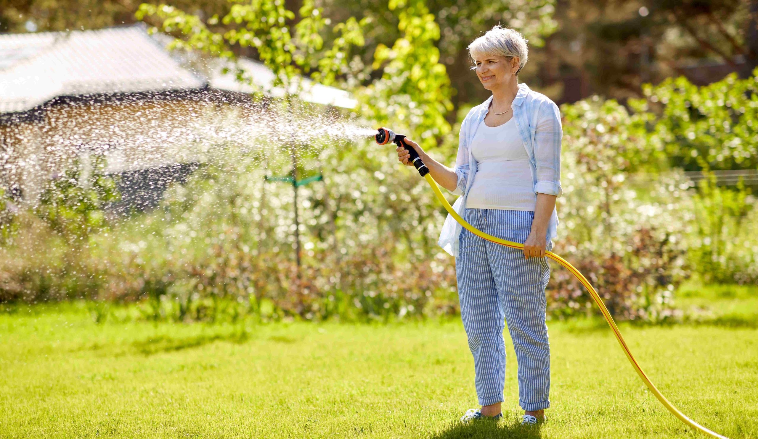 középkorú nő locsolja a füvet