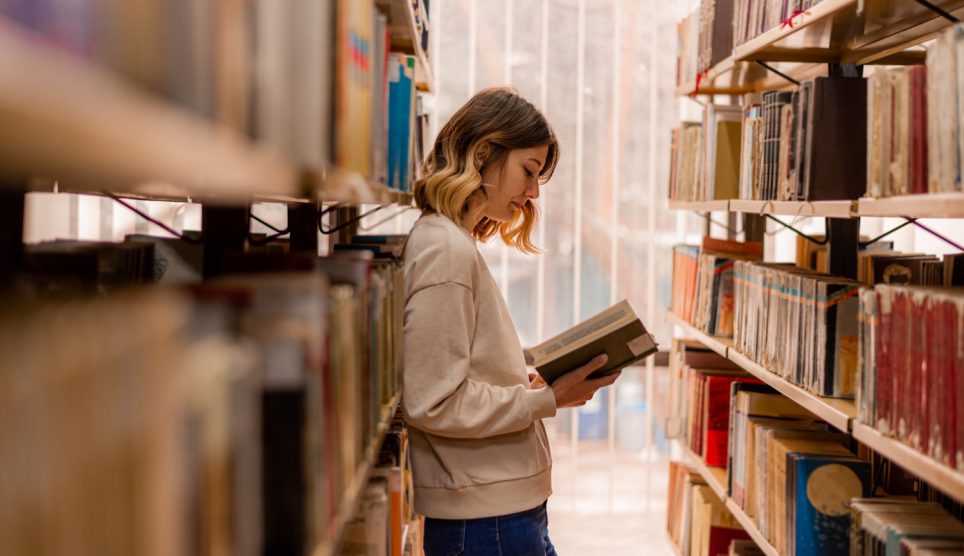 fiatal nő könyvtárban könyvet lapozgat
