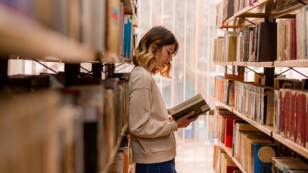 fiatal nő könyvtárban könyvet lapozgat