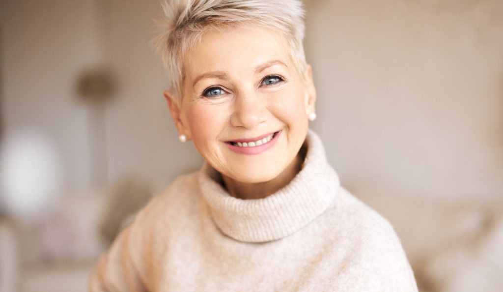 szép idős nő garbóban pasztel színek mosolyog