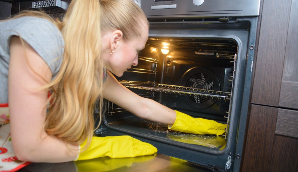 szőke nő a koszos sütőt takarítja