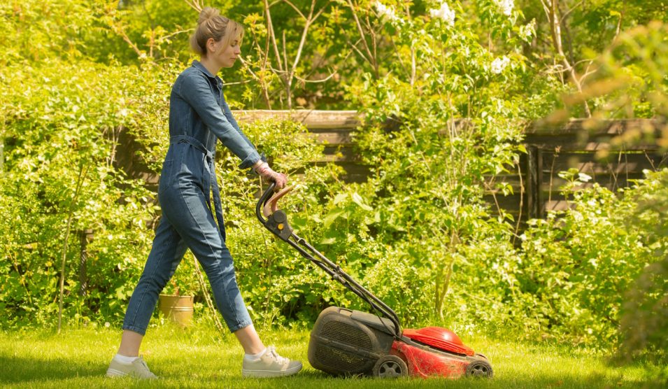 tavasszal füvet nyír a akertben egy csinos nő