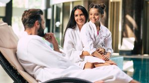 Boldog pár a kislányukkal fürdőköpenyben ülnek a wellness szállodában a medence mellett