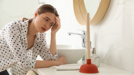 kétségbeesett nő áll az eldugult mosdó mellett pumpával