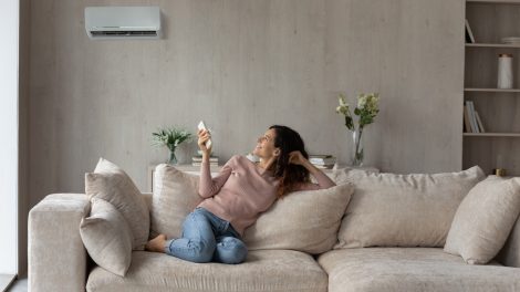 Egy nő ül a kanapén és kapcsolgatja a klímát