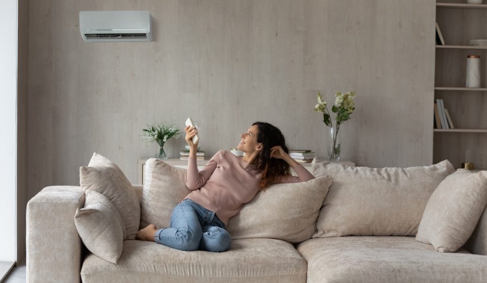 Egy nő ül a kanapén és kapcsolgatja a klímát