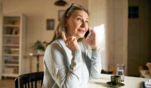 középkorú nő telefonál otthon a konyhaasztalnál