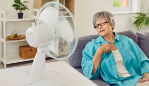 Idősebb hölgy ül a ventilátor előtt