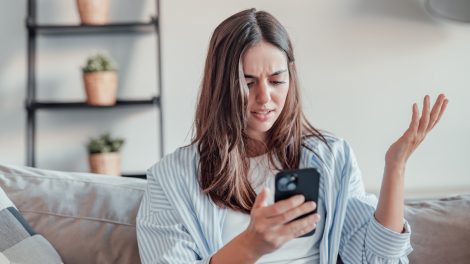tanácstalan nő a mobiltelefonját nézi a kanapén ülve