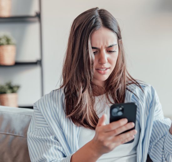 tanácstalan nő a mobiltelefonját nézi a kanapén ülve
