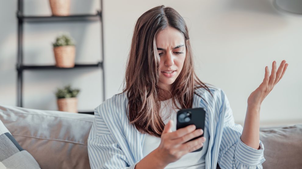 tanácstalan nő a mobiltelefonját nézi a kanapén ülve