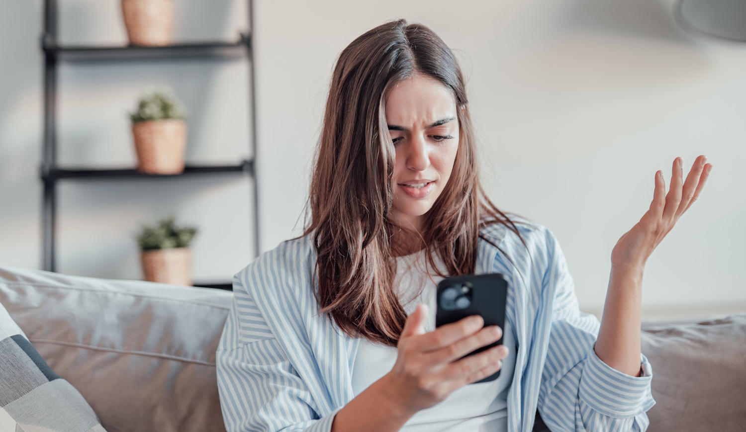 tanácstalan nő a mobiltelefonját nézi a kanapén ülve