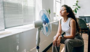 nő kánikulában ventillátorozik a nappaliban