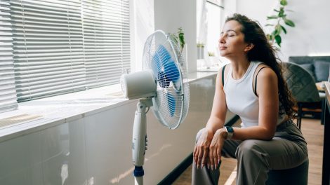 nő kánikulában ventillátorozik a nappaliban