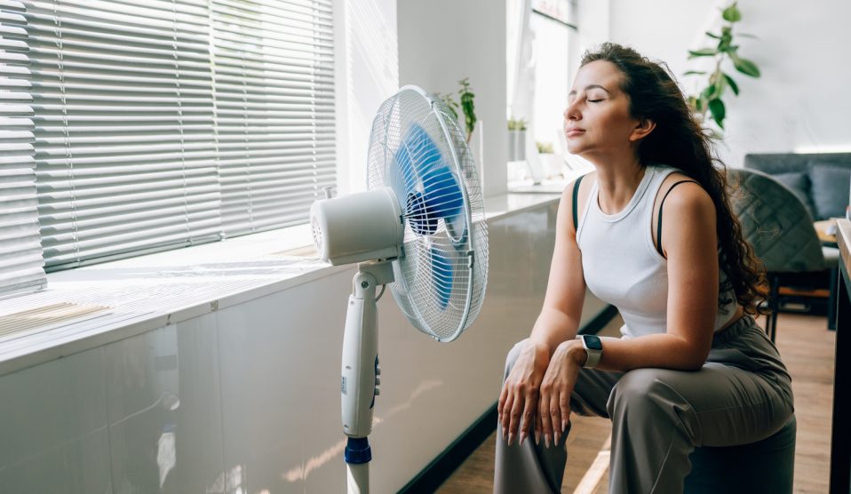 nő kánikulában ventillátorozik a nappaliban