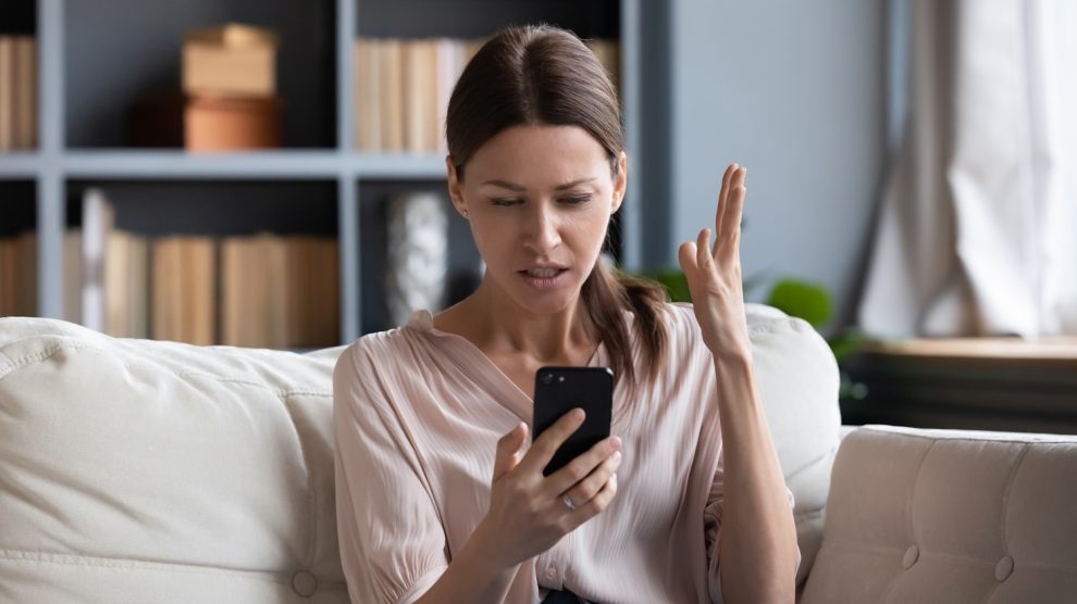 aggódó nő a kanapén a telefonját nézi
