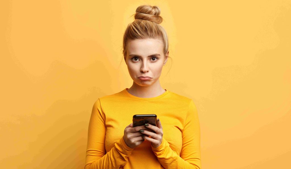 Nő sárga háttér előtt áll a telefonjával