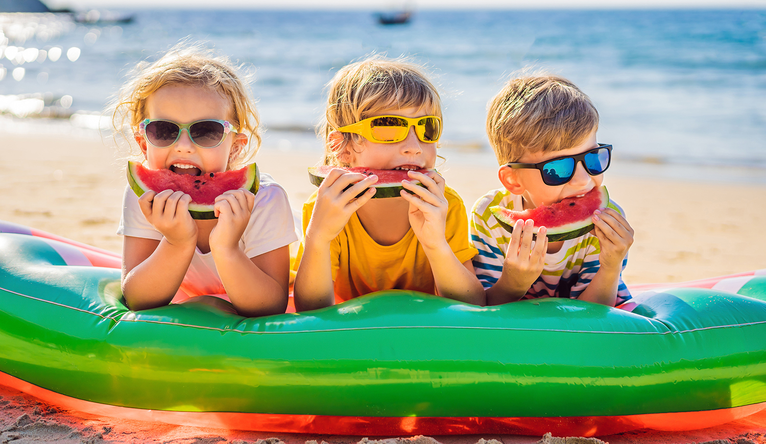 Gyerekek napszemüvegben görögdinnyét esznek a strandon