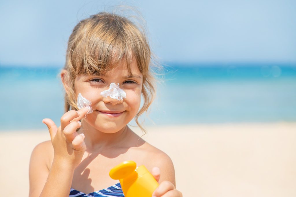 Sunscreen on the skin of a child Selective focus | Meglepetés kislány keni be magát naptejjel a tengerparton