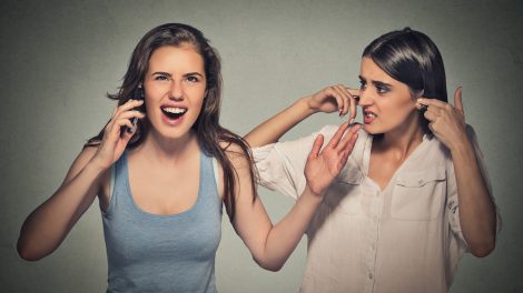 nő hangosan telefonál másik nő befogja a fülét mellette