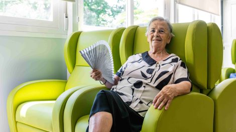 Nagymama legyezi magát egy zöld fotelben