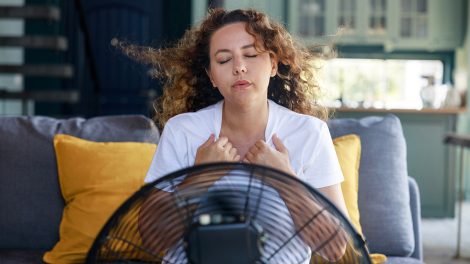 Nő élvezi a ventilátor hűvös levegőjét otthon