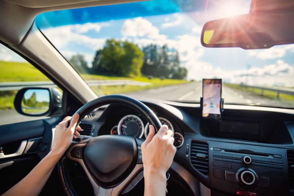Autót vezető nő, aki okostelefont használ navigációhoz