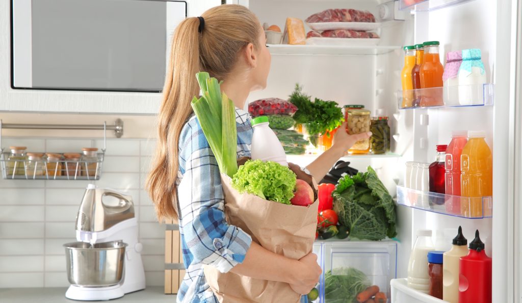 Woman putting products into refrigerator in kitchen | Meglepetés szőke nő zöldségeket tesz be a hűtőbe nyári bevaásárlásból