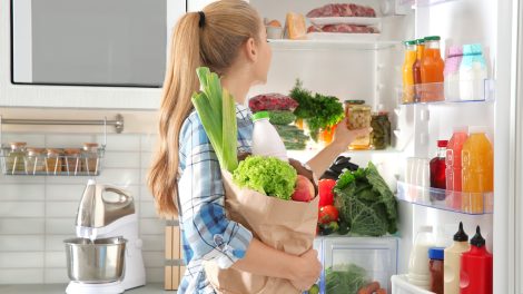 szőke nő zöldségeket tesz be a hűtőbe nyári bevaásárlásból