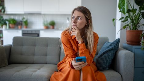 nő aggódva ül a kanapén, kezében mobiltelefon