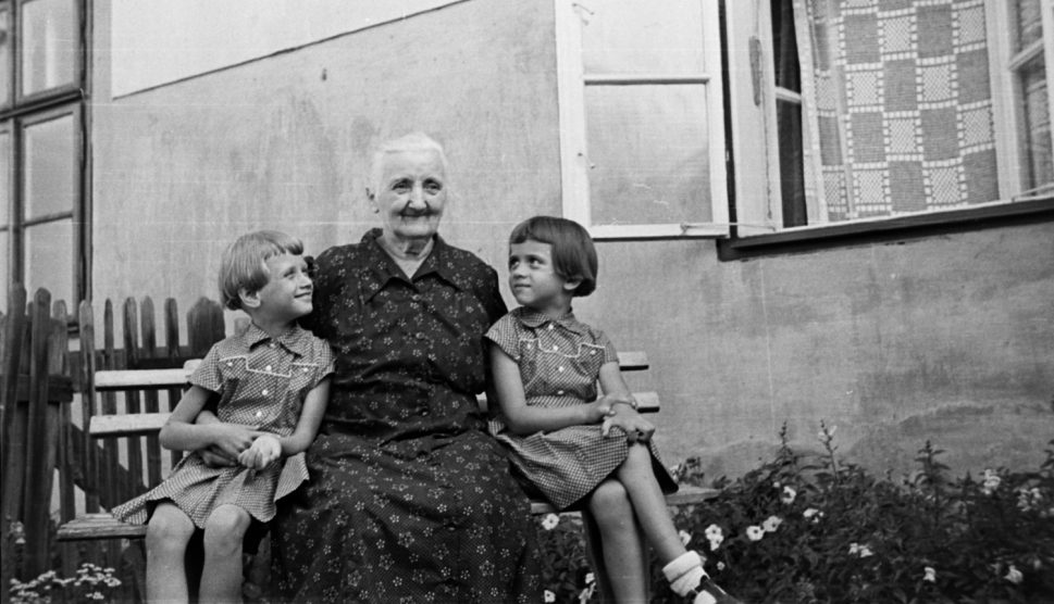 fekete fehér kép az 1950-es évekből nagymama ül a lócán két kislány unokájával