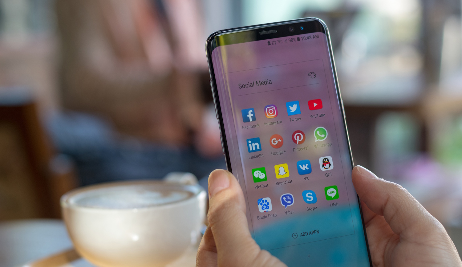 samsung mobiltelefont tart a kezében egy nő egy kávézóban