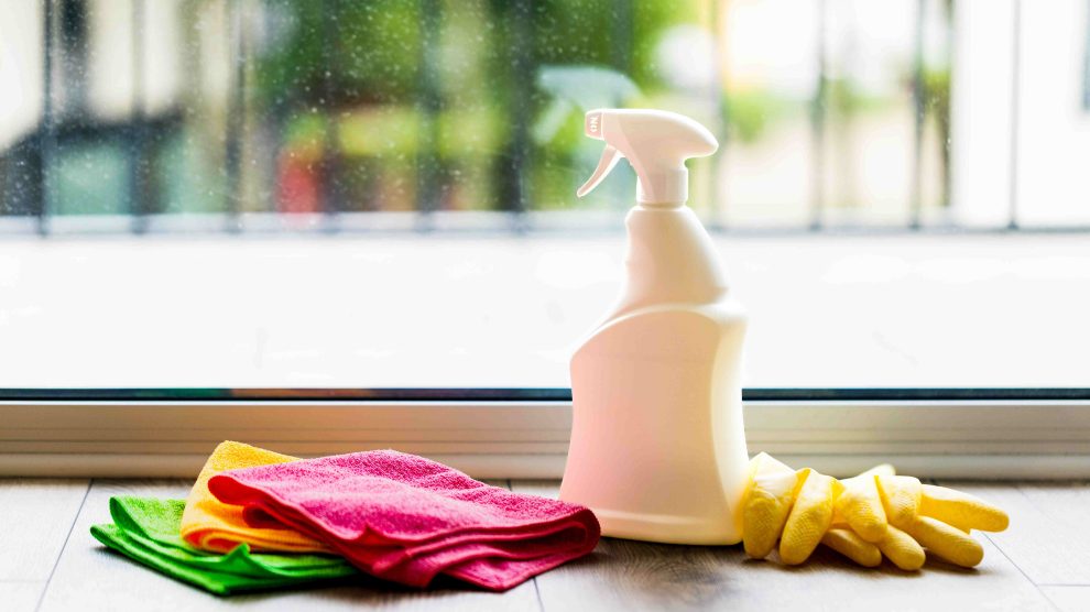 Egy üveg tisztítószer-spray és törlőkendők koszos ablak előtt