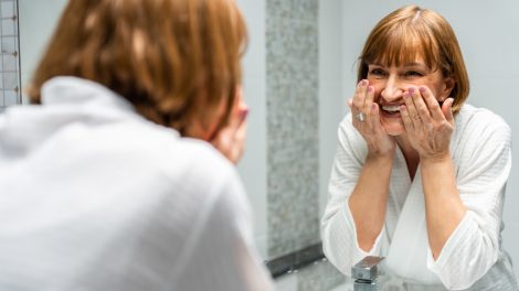 60+-os szép bőrű nő arcot mos a fürdőszobában