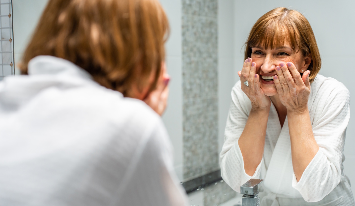 60+-os szép bőrű nő arcot mos a fürdőszobában