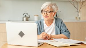 Idős nő ül a laptop előtt és mosolyog